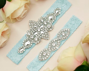 Pode incluir: Duas ligas azuis claras com enfeites de strass prateados. O enfeite maior é um design floral e o enfeite menor é um design curvo.