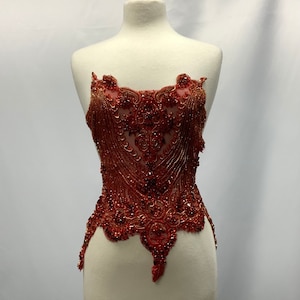 May include: A red beaded applique with a floral design. The applique is on a white mannequin and is about 12 inches tall.