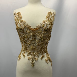 May include: Gold beaded and sequined applique with a floral design. The applique is on a white background.