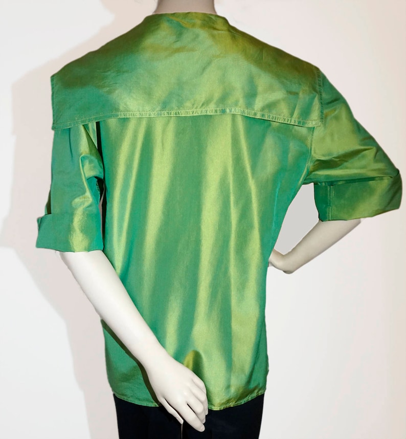 May include: A green, silky, short-sleeved shirt with a high collar and a large, folded collar. The shirt has a slightly gathered look and a sheen.
