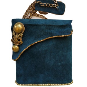 May include: A teal handbag with a gold chain strap and decorative gold accents. The rectangular bag has a curved flap with gold beading and a large, ornate gold embellishment. The bottom edge is trimmed with gold rope.