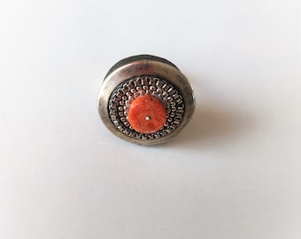 Anillo único de metal blanco sobre plataforma negra con coral.