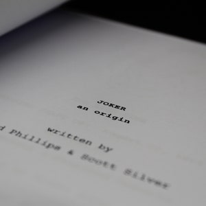 May include: A close-up of a script page for the movie "Joker: An Origin." The script is written by Todd Phillips and Scott Silver.