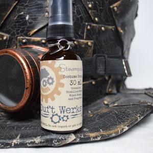 Puede incluir: Botella de vidrio marrón de "Steampunk Costume Scent" con pulverizador, 30 ml. La botella se encuentra sobre un sombrero de cuero negro desgastado con gafas de color cobre. La etiqueta incluye el texto "Duft Werks".