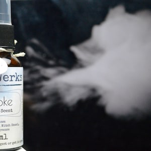 May include: A small brown glass bottle with a white label that reads "Duft werks Smoke Costume Scent". The label also includes the text "Contains Distilled Water, Witch Hazel and Fragrance" and "30 ml".