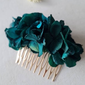 Puede incluir: Un peine para el cabello de metal dorado adornado con una flor de hortensia azul verdoso. El peine tiene un diseño decorativo con una fila de dientes.