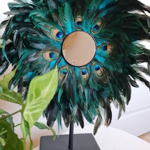 Peut inclure: Un miroir décoratif avec un cadre rond en plumes bleu sarcelle et noires. Le miroir est monté sur un pied noir.