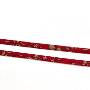 May include: Two red fabric straps with a floral pattern in beige and brown. The straps are thin and appear to be made of a lightweight material, possibly for a craft or accessory.