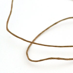 Puede incluir: Primer plano de un cordel de yute marrón, enrollado y anudado sobre un fondo blanco.