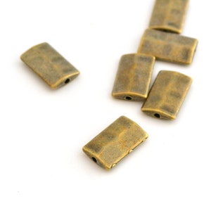 Peut inclure: Un groupe de huit perles rectangulaires en métal de couleur or antique avec un trou au centre.