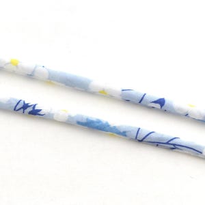 Peut inclure: Gros plan sur deux lanières de tissu à motifs floraux. Les lanières sont bleu clair avec des fleurs blanches et jaunes et des accents bleu foncé. Les lanières sont sur fond blanc.