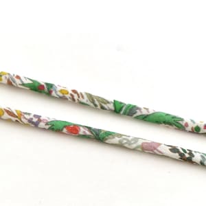 Peut inclure: Deux cordons fins à motifs floraux, sur fond blanc. Les cordons présentent une base blanche ornée de détails floraux verts, rouges, jaunes et violets. L'image offre une vue rapprochée des cordons en tissu.