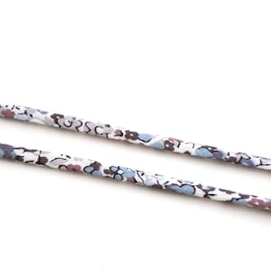 Peut inclure: Deux cordons à motifs floraux sur fond blanc. Les cordons présentent un motif répétitif de petites fleurs et feuilles bleues, violettes et grises. Les cordons sont fins et semblent être en tissu.