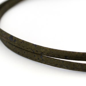 Puede incluir: Primer plano de un cordón verde oscuro hecho de corcho con un sutil patrón de motas azules. El cordón está cosido a lo largo de los bordes.
