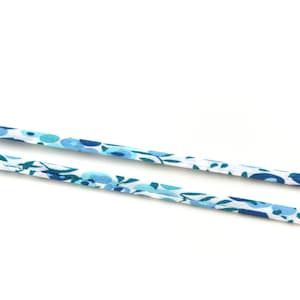 Peut inclure: Deux bandes de tissu à motifs floraux dans les tons de bleu et de blanc. Le tissu semble être un coton léger ou une matière similaire, avec de petits motifs stylisés de fleurs et de feuilles.