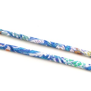 Peut inclure: Deux cordons en tissu avec un motif floral dans les tons de bleu, vert et blanc. Les cordons sont positionnés en diagonale sur un fond blanc, mettant en valeur l'imprimé détaillé et les variations de couleurs.