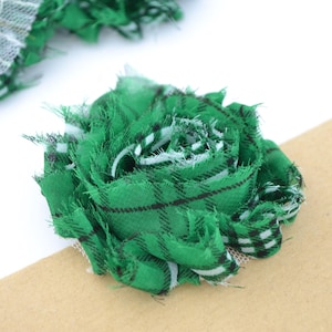 Peut inclure: Gros plan sur des fleurs en tissu faites à la main. Les fleurs sont faites de tissu à carreaux vert avec des accents blancs et noirs. Une fleur est mise au point, une autre est partiellement visible en arrière-plan. Les fleurs sont sur une surface blanche et beige.