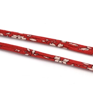 Puede incluir: Cordón de tela con estampado floral rojo y blanco. El cordón está doblado por la mitad y los extremos son visibles.