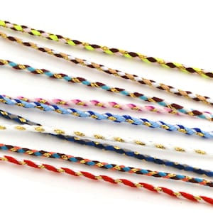 May include: Close-up of several colourful braided cords with gold metallic accents. The cords are in various colours, including red, blue, white, and yellow. The cords are likely used for jewellery making or crafts.