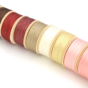 Peut inclure: Plusieurs bobines de fil de différentes couleurs, dont bleu marine, marron, rouge et rose. Les bobines sont en bois et disposées en diagonale, parfaites pour les projets de couture et d'artisanat.