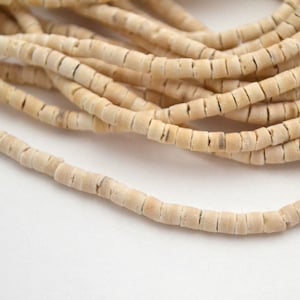 Könnte beinhalten: Eine Schnur aus cremefarbenen Muschelkernperlen. Die Perlen sind klein und rund, mit einer leicht unregelmäßigen Form. Sie sind auf einer dünnen Schnur aufgefädelt.