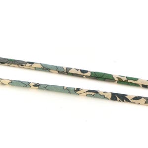 Puede incluir: Primer plano de un cordón de tela beige y verde con estampado. El cordón está doblado por la mitad y el estampado es visible en ambos lados.