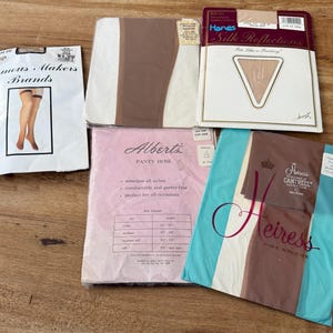 Puede incluir: Un surtido de medias vintage en su embalaje original. Las marcas incluyen Famous Makers, Hanes Silk Reflections, Alberts Panty Hose y Heiress Fine Nylons. Los colores van del nude al marrón, con imágenes de las medias en algunos paquetes.