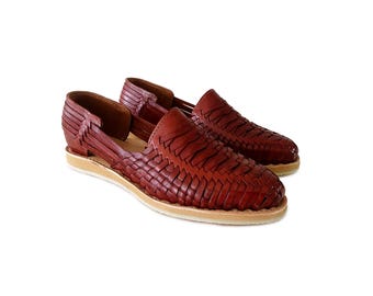 May include: A pair of dark brown leather huarache shoes featuring a woven upper design with interlaced leather strips, an open side construction, and a flat, light-colored rubber sole. The shoes have a rounded toe and a low-cut heel.