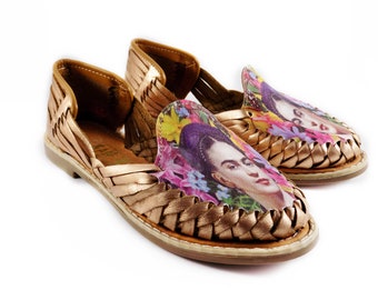 Pode incluir: Um par de sandálias de couro dourado com um design tecido. As sandálias apresentam uma estampa floral com um retrato de Frida Kahlo.