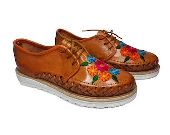 Könnte beinhalten: Ein Paar braune Lederschuhe mit bunter Blumenstickerei. Die Schuhe haben ein gewebtes Design an der Sohle und eine weiße Gummisohle.
