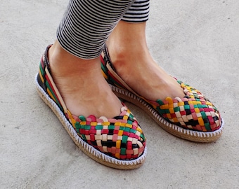 May include: A pair of colourful woven leather espadrille flats with a white rope trim. The shoes have a multi-coloured woven pattern with shades of green, red, yellow, and black.
