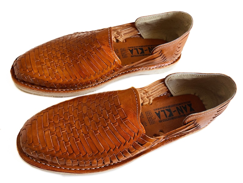 K&ouml;nnte beinhalten: Ein Paar braune Ledersandalen mit gewebtem Muster. Die Sandalen haben einen Lederriemen &uuml;ber dem Fu&szlig;r&uuml;cken und eine Ledersohle. Der Markenname "YAN-KLA" ist auf der Innenseite der Sandalen sichtbar.