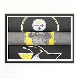 May include: Three stacked t-shirts with different designs. The top shirt is black with a yellow and black Pittsburgh Steelers logo. The middle shirt is gray with a yellow and black pirate logo. The bottom shirt is black with a yellow and black penguin logo.