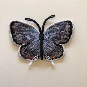 May include: A blue and gray embroidered butterfly patch with black outlines and orange accents.