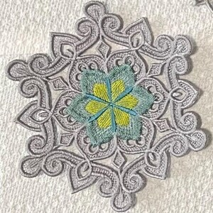 May include: A silver snowflake-shaped lace doily with a blue and yellow flower in the center.