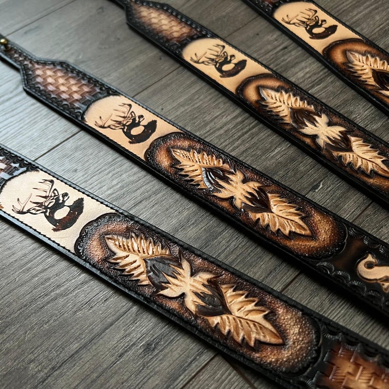 May include: Four brown leather gun slings with a deer head design and intricate tooling. The slings are made of a dark brown leather with a light brown background.