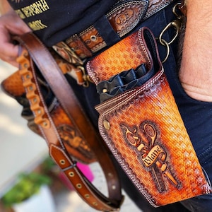 Peut inclure: Une ceinture en cuir marron avec deux porte-outils. Le porte-outils de droite est orné d'un motif de ciseaux et du mot "Blaine".