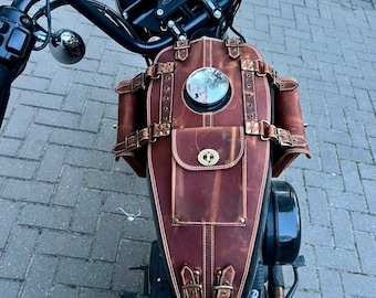 May include: A brown leather motorcycle tank bag with a small pocket and decorative buckles. The bag is mounted on a black motorcycle, with a speedometer and handlebars visible in the background. The bag has a round mirror.