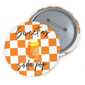 May include: Orange soda can with the text "Sweet as soda pop" on a white and orange checkered background. The button is a round pinback.