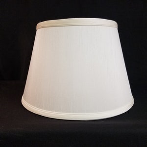 May include: A white lampshade with a slightly rounded top and a white trim around the bottom edge.