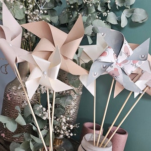 Peut inclure: Quatre moulinets en papier de différentes couleurs et motifs. Les moulinets sont sur des bâtonnets en bois et sont disposés dans un vase avec de la verdure.