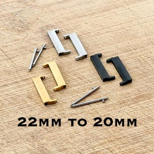 May include: Watch strap adapters in silver, gold, and black, shaped like the letter "L", scattered on a wooden surface. The text "22MM TO 20MM" is printed in black.