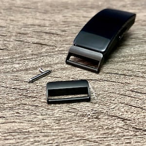 Puede incluir: Correa de reloj negra con hebilla y pasador de resorte. La correa está hecha de un material negro liso.