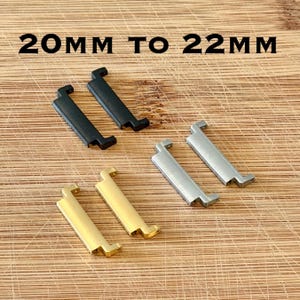 May include: An assortment of watch band adapters in black, silver, and gold. The text "20MM TO 22MM" is displayed at the top. The adapters are rectangular with a curved hook and a notched base, designed for watch bands.