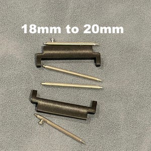 May include: Black watch band adapters and silver spring bars are displayed against a gray background. The text "18mm to 20mm" is printed in white. The image shows watch band components.