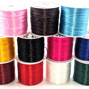 May include: A collection of spools of elastic cord in various colors, including pink, brown, blue, yellow, black, fuchsia, navy, burgundy, red, white, and green. The spools are neatly arranged, showcasing the vibrant hues of the elastic cord.