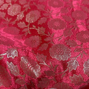 Puede incluir: Tela roja con un patrón floral dorado. La tela es texturizada y tiene un ligero brillo.