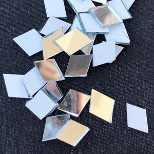 May include: A pile of small diamond-shaped mirror tiles with adhesive backing. The tiles are silver and gold.