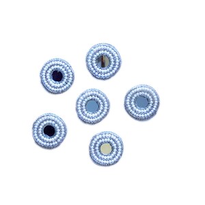 Puede incluir: Seis pequeños espejos redondos con bordes de cuentas de perlas blancas. Los espejos están dispuestos en un patrón circular sobre un fondo blanco.