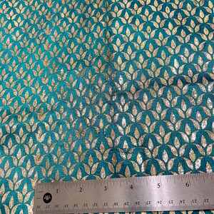 May include: Teal fabric with a gold leaf pattern. The fabric is measured with a ruler showing 6 inches.